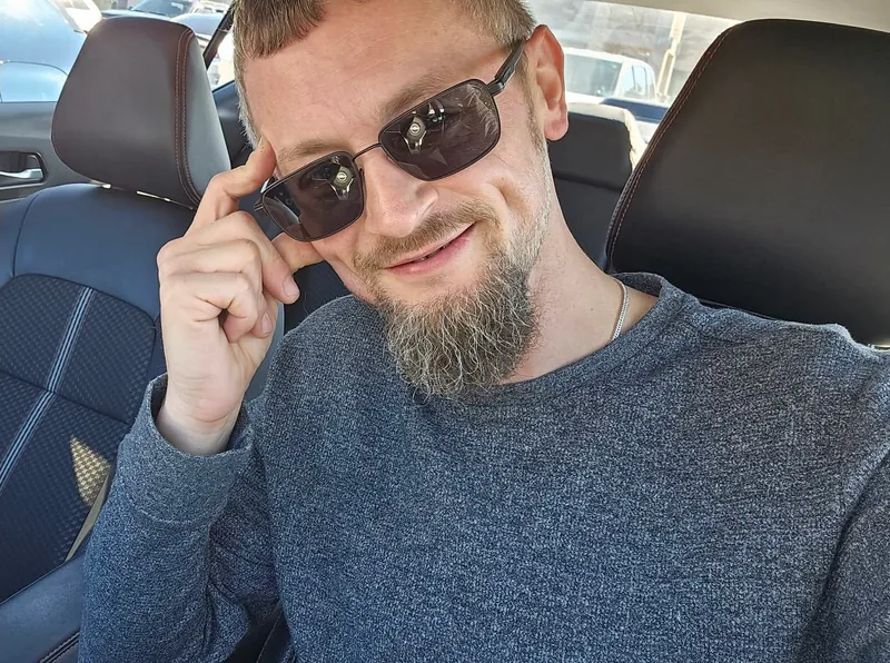 Erin in a car seat, sunglasses tipped down, smiling at the camera.