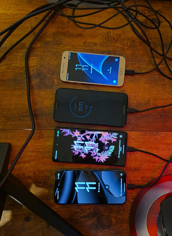 Four Android phones connected by USB on a wooden desk, from the Galaxy S7 to a newer Pixel.